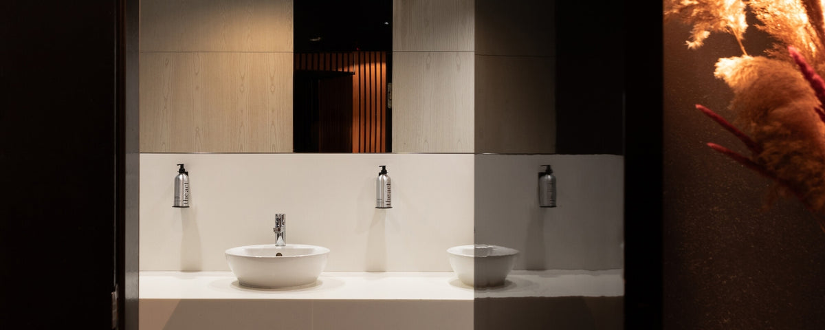 Hotel washroom with The Act Zest of Verbena hand wash bottles mounted in wall dispenser holders