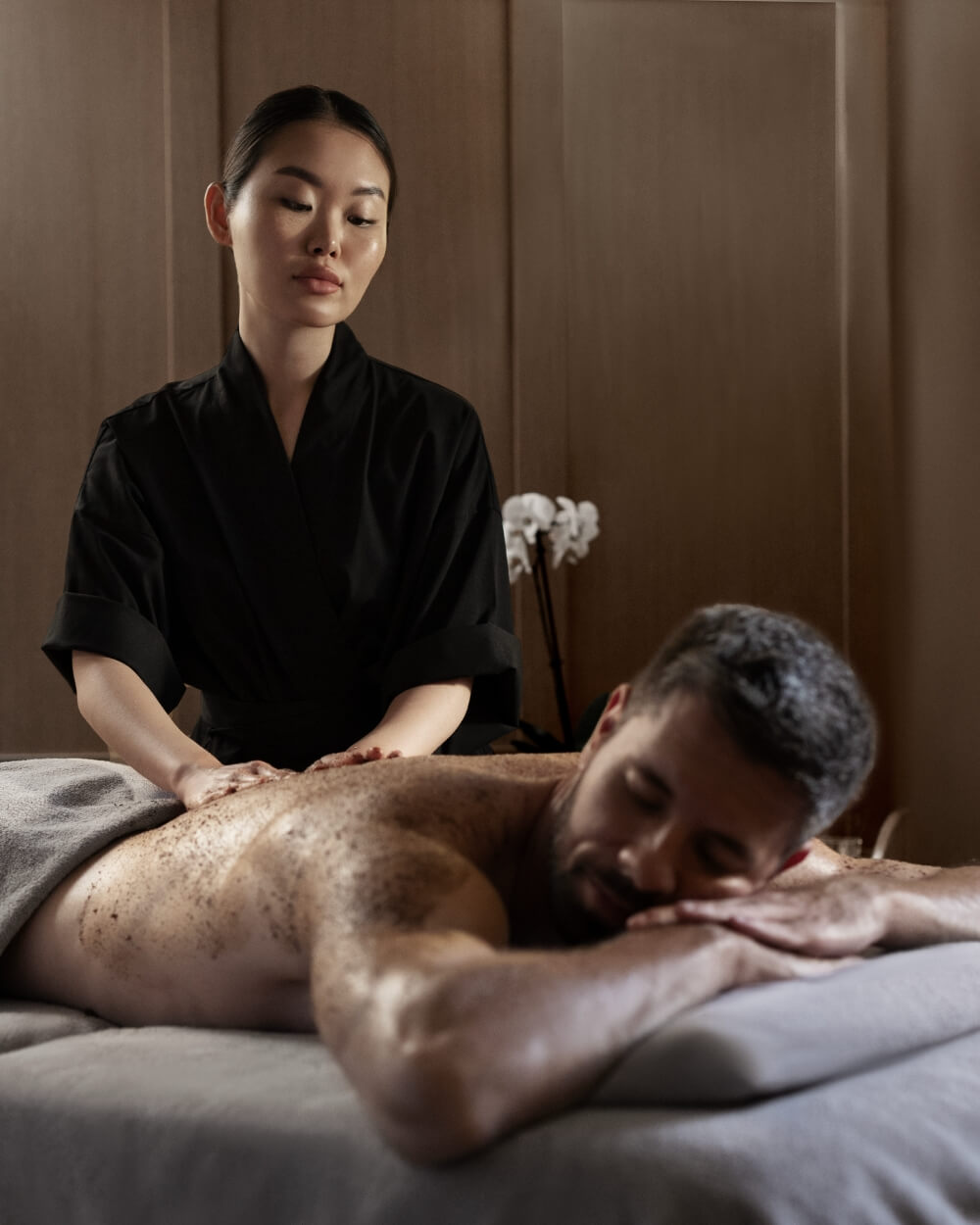 Spa therapist performing a body scrub treatment using The Act Cocoa and Coffee Scrub
